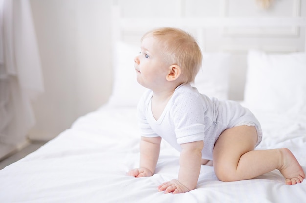 Mignon petit garçon souriant apprend à ramper sur un lit blanc à la maison petit bébé blond s'est réveillé le matin enfance et famille heureuses