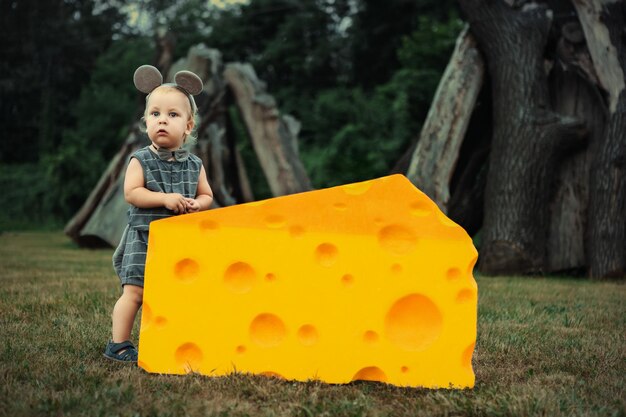Mignon petit garçon souris jouant avec un gros morceau de fromage sur l'herbe