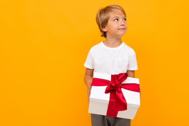 Mignon petit garçon en t-shirt et pantalon détient une boîte avec un cadeau lui-même isolé sur jaune