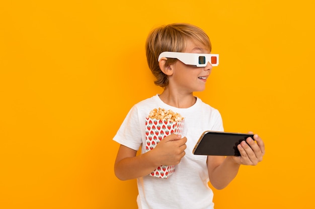 Mignon petit garçon en t-shirt et pantalon regarder des films avec smartphone isolé sur jaune