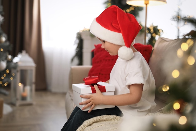 Mignon petit garçon tenant une boîte-cadeau sur un canapé dans une chambre décorée pour Noël