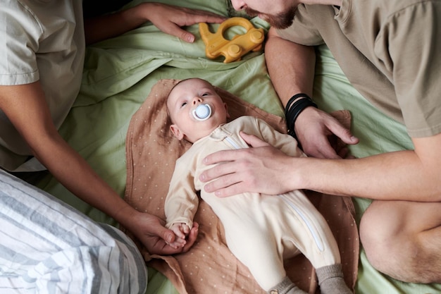 Mignon petit garçon avec tétine dans sa bouche allongé sur le lit entre la mère et le père