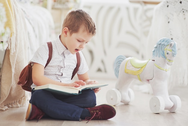 Le mignon petit garçon va à l'école pour la première fois. Enfant avec sac et livre. Kid fait une mallette, chambre d'enfant sur un fond