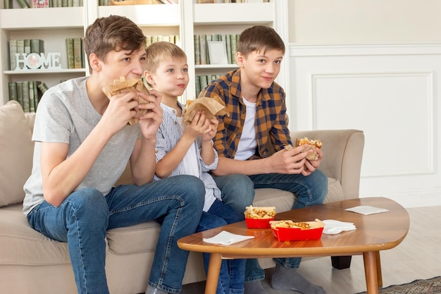 Un mignon trois adolescents mangeant de la restauration rapide dans le salon regarder la télévision