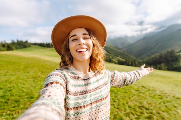 Un mignon voyageur avec un chapeau prend un selfie sur fond de paysages de montagne verts Concept de liberté