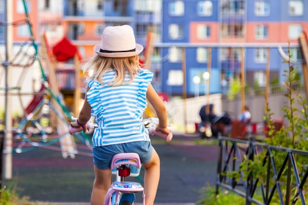 Mignonne adorable petite fille blonde par derrière aime faire du petit vélo par chemin dans un parc d'été vert dans le parc de la ville