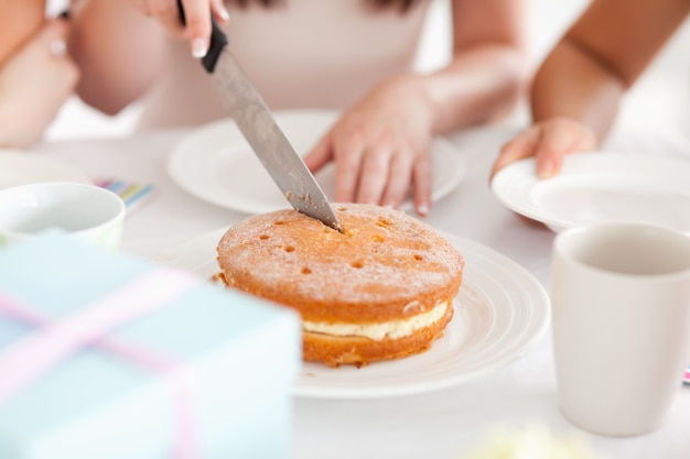 Mignonne femme assise à une table en train de couper un gâteau