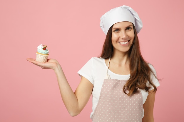 Mignonne femme au foyer chef cuisinier pâtissier boulanger en t-shirt blanc, chapeau de chefs toque cuisson tenir doux isolé sur fond pastel rose en studio. Processus de fabrication de cupcakes. Maquette du concept de nourriture de l'espace de copie.