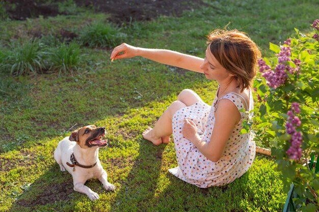 Mignonne jeune femme mince joue avec son chien drôle bien-aimé dans la cour par une journée d'été ensoleillée. Beau