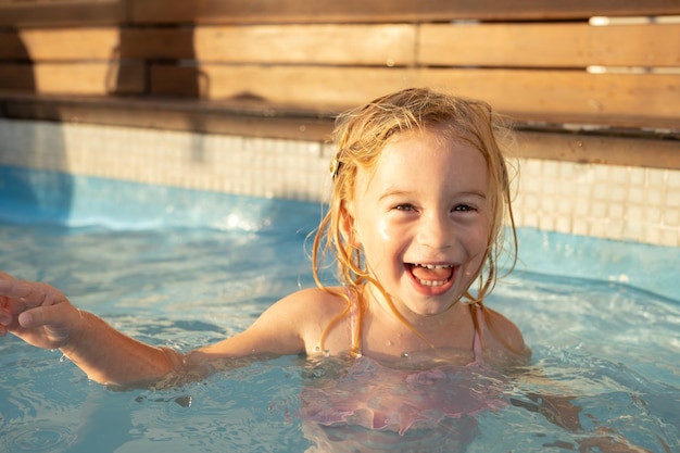 Mignonne jolie riante heureuse caucasienne blonde fille de deux ans enfant enfant en bas âge s'amusant avec de l'eau regardant la caméra en plein air en été près de la piscineEnfance insouciantemode de vie de loisirs