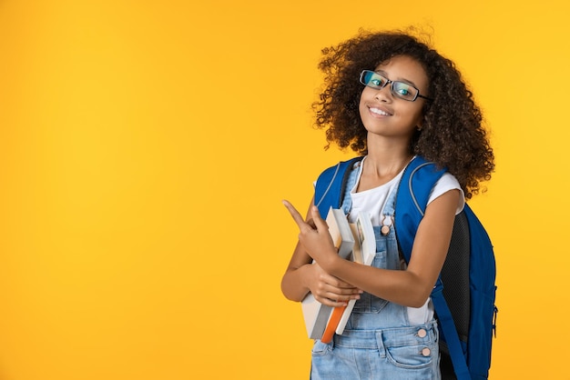 Mignonne petite écolière afro-américaine souriante avec des livres sur fond jaune