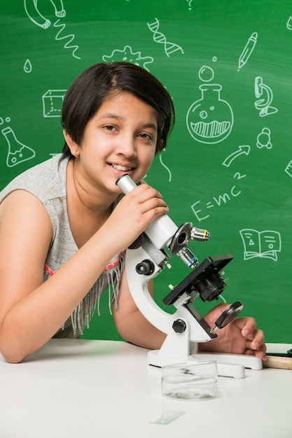 Mignonne petite écolière asiatique indienne expérimentant ou étudiant la science en laboratoire, sur fond de tableau vert avec des griffonnages éducatifs