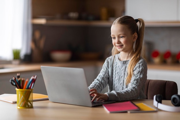 Mignonne petite écolière étudie avec un ordinateur portable à la maison en tapant sur le clavier de l'ordinateur