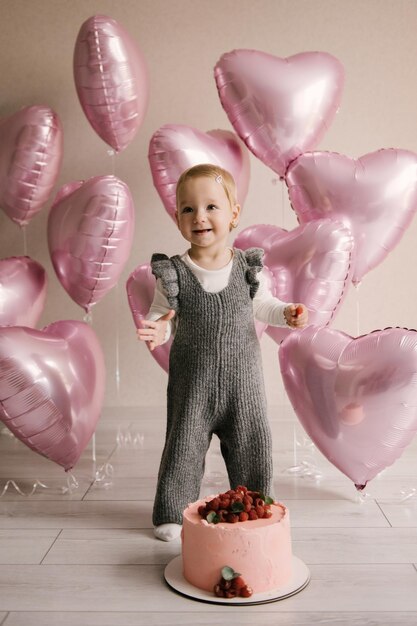 Mignonne petite fille 1er anniversaire bébé avec des ballons coeur rose et un gâteau d'anniversaire