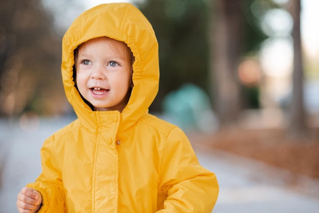 Mignonne petite fille de 2 à 3 ans portant une veste de pluie jaune avec capuche dans le parc d'automne en plein air saison d'automne