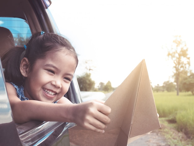 Mignonne Petite Fille Asiatique S'amuser à Jouer Avec Un Avion En Papier Jouet Hors De La Fenêtre De La Voiture