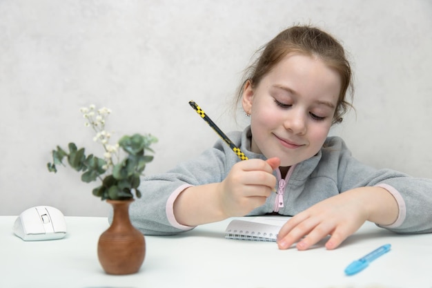 Mignonne petite fille assise à la table souriante écrivant avec un crayon dans un cahier apprenant la rentrée scolaire