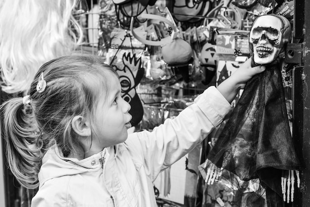 Mignonne petite fille attrapant un squelette devant la boutique pendant les célébrations d'Halloween Concept d'entreprise d'Halloween et concept de consommation Noir et blanc