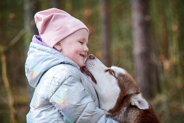 Mignonne petite fille au chapeau rose et veste bleu clair étreint le chien Husky de Sibérie et souriant