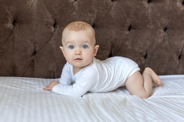 Photo mignonne petite fille en bas âge se trouve sur le lit à la maison et regarde la caméra avec le sourire