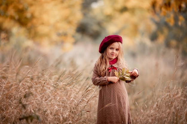 Mignonne petite fille blonde aux cheveux longs en automne dans le parc sourit et profite d'une journée ensoleillée et du beau temps