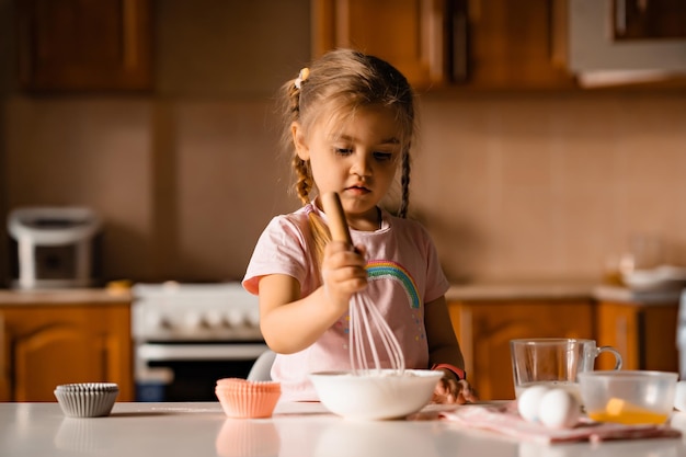 Mignonne petite fille blonde faisant cuire la pâte dans la cuisine à la maison