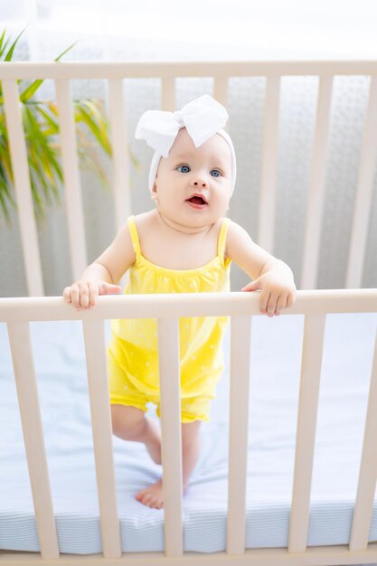 Mignonne petite fille en bonne santé est debout dans un berceau le matin en regardant la caméra le concept de produits pour bébés le concept de sommeil de bébé