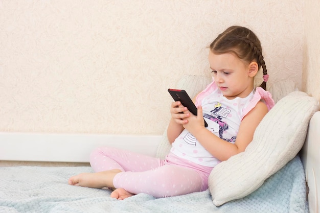 Mignonne petite fille caucasienne se trouve et utilise un smartphone moderne