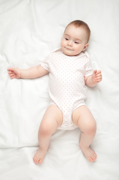 Mignonne petite fille couchée et sourire sur lit blanc.