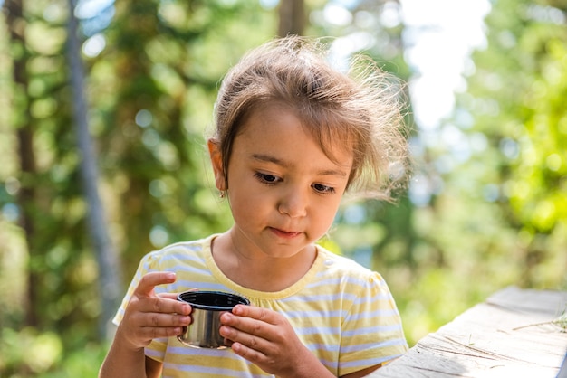 mignonne petite fille dans une forêt d'été tenant une tasse de thé et souriant