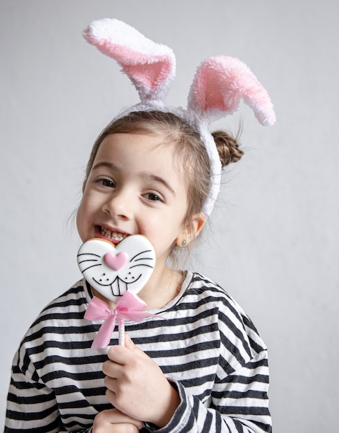 Mignonne petite fille avec du pain d'épice de Pâques sur un bâton et des oreilles de lapin décoratives sur sa tête.