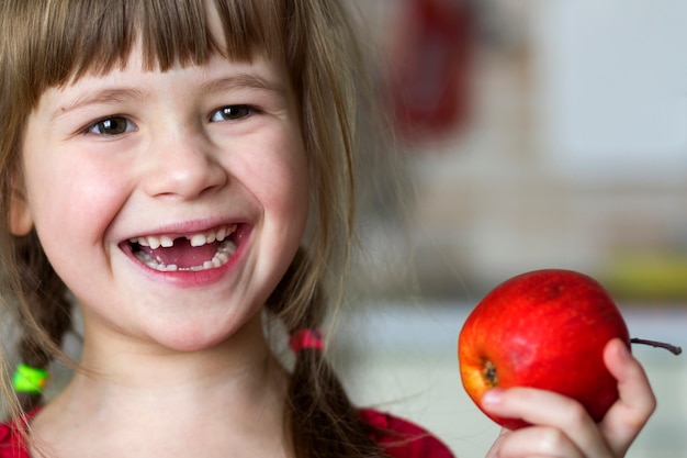 Une mignonne petite fille édentée bouclée sourit et tient une pomme rouge.