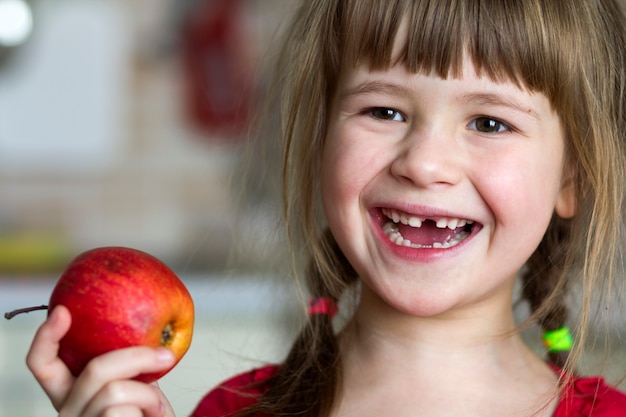 Une mignonne petite fille édentée bouclée sourit et tient une pomme rouge.