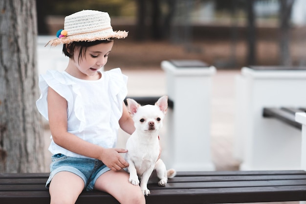 Mignonne petite fille élégante assise avec un chien dans un parc à l'extérieur