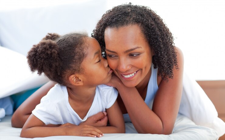 Photo mignonne petite fille embrasse sa mère couchée sur le lit