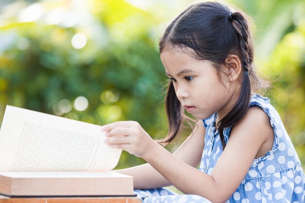 Mignonne petite fille enfant asiatique lisant un livre à l&#39;extérieur dans le fond de la nature