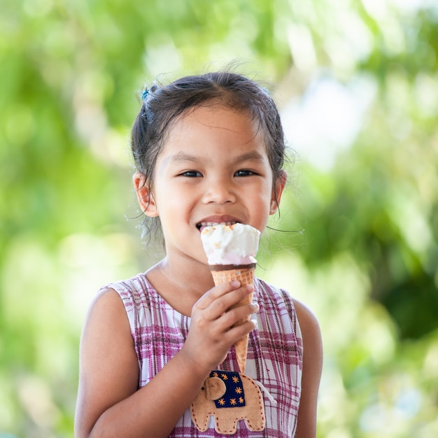 Mignonne petite fille enfant asiatique mange délicieux cône de glace avec plaisir et bonheur