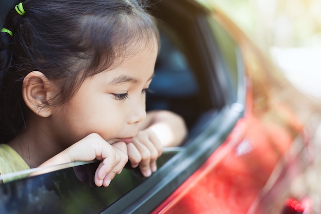 Mignonne petite fille enfant asiatique voyageant en voiture et en regardant par la fenêtre de la voiture
