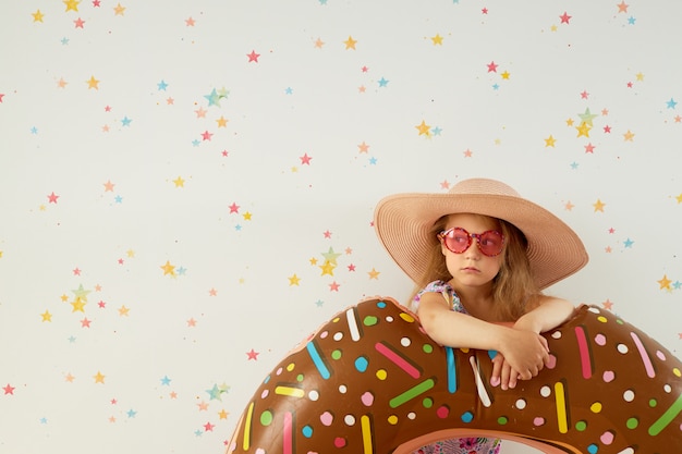 Mignonne petite fille enfant au chapeau avec anneau gonflable sur mur de couleur. Quarantaine de vacances d'été à la maison