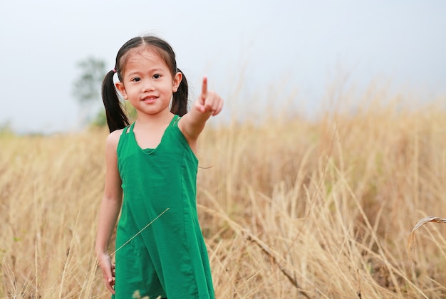 Mignonne petite fille enfant pointant vers vous dans le champ de l&#39;été en plein air