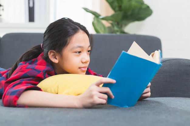 Mignonne petite fille enfant en tenue décontractée lisant un livre allongé sur un canapé dans le salon