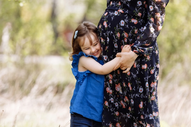 Mignonne petite fille étreignant et embrassant le ventre de femme enceinte de sa mère au printemps nature