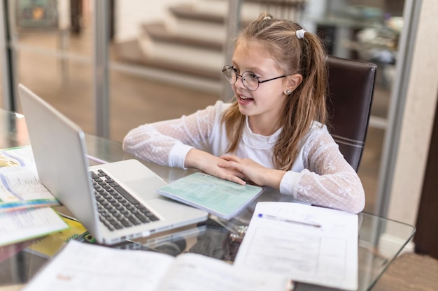 Mignonne petite fille faisant sérieusement ses devoirs à l'aide d'un ordinateur portable à la maison pour l'éducation en ligne, les études à domicile et la communication en ligne Apprentissage à distance pour les enfants Distance sociale Rester à la maison