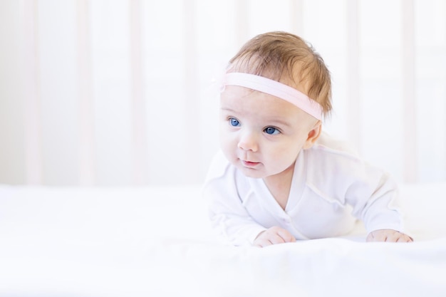 Mignonne petite fille gros plan sur un lit sur un lit en coton blanc allongé sur le ventre et apprenant à tenir sa tête portrait d'un drôle de petit bébé nouveau-né à la maison dans un berceau en gros plan