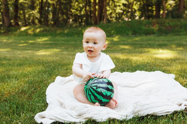 Mignonne petite fille heureuse avec un ballon est assise sur l'herbe verte dans le parc