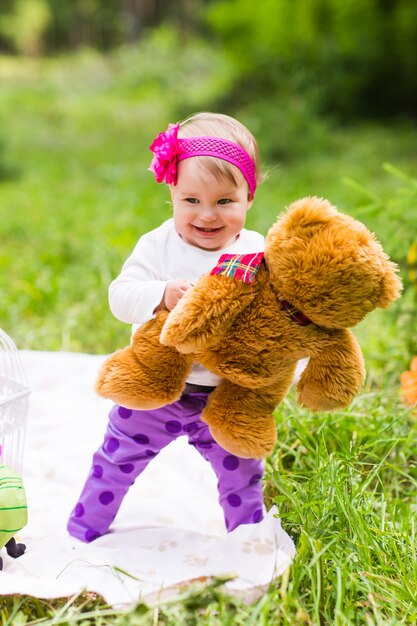 Mignonne petite fille heureuse avec gros ours en peluche brun sur la prairie d'herbe verte, au printemps ou en été.