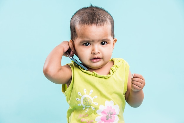 Mignonne petite fille indienne ou asiatique utilisant un smartphone et appelant la mère assise isolée sur fond bleu