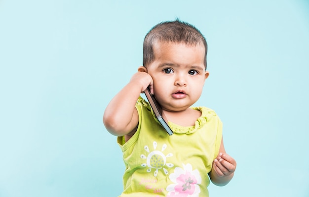 Mignonne petite fille indienne ou asiatique utilisant un smartphone et appelant la mère assise isolée sur fond bleu