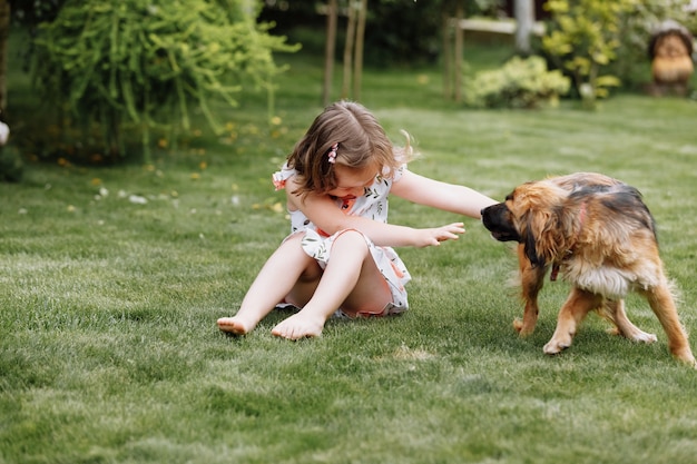 Une mignonne petite fille joue avec son chien à l'extérieur sur l'herbe à la maison