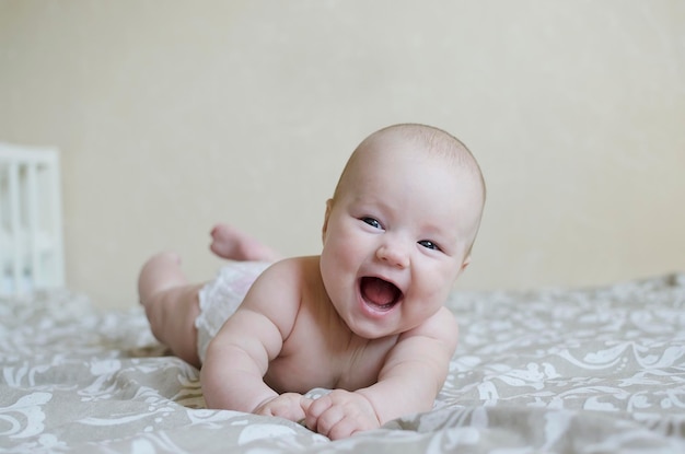 Mignonne petite fille sur le lit en gros plan se trouve sur le ventre et sourit en riant Enfance heureuse